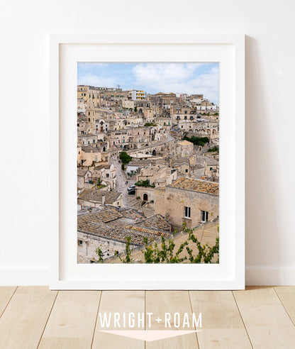 Historic stone buildings and textured streets in Matera, Italy with soft blue sky in a vertical architectural photograph.