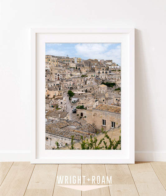 Historic stone buildings and textured streets in Matera, Italy with soft blue sky in a vertical architectural photograph.