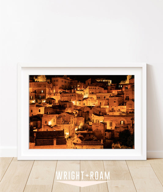 Framed photograph of Matera, Italy at night with glowing amber streetlights and historic stone buildings.