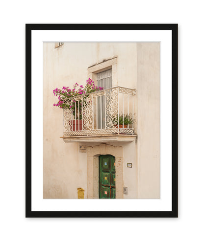 A minimalist fine art photograph in black frame featuring a textured beige wall, window, and iron balcony in Puglia, Italy.