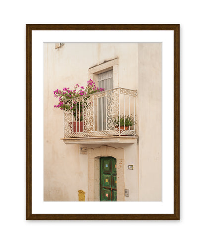 A minimalist fine art photograph in dark wood frame featuring a textured beige wall, window, and iron balcony in Puglia, Italy.