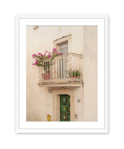 A minimalist fine art photograph in white frame featuring a textured beige wall, window, and iron balcony in Puglia, Italy.