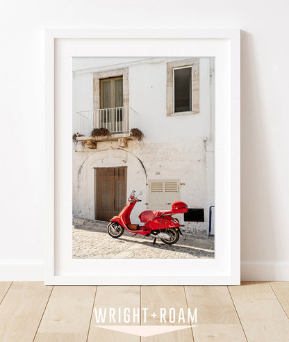 A framed fine art photograph of a historic Puglia building in soft neutral tones, accented by a classic red moped.