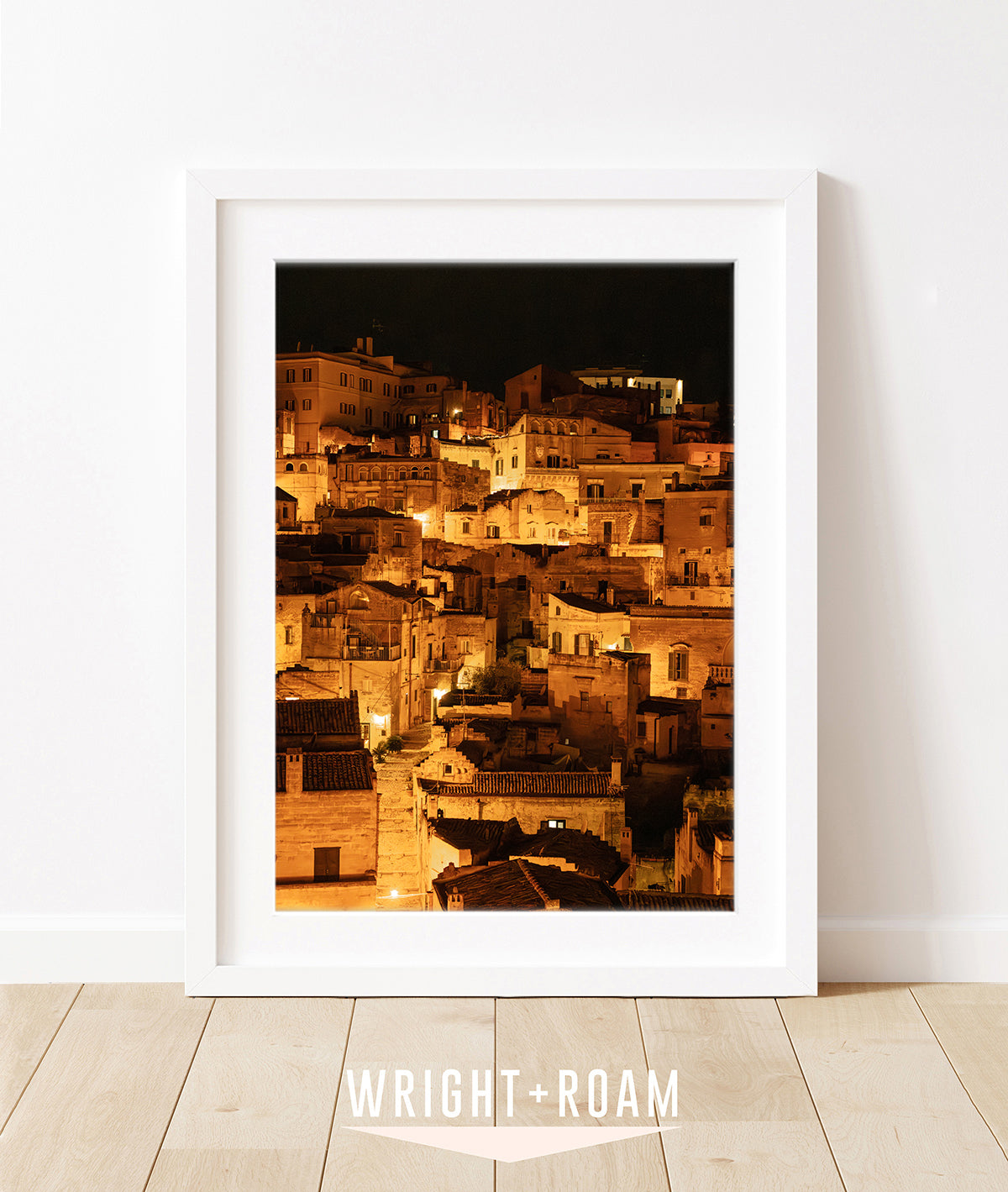 framed photograph of Historic city of Matera, Italy at night with glowing amber lights and dark stone architecture in a vertical cityscape photograph.