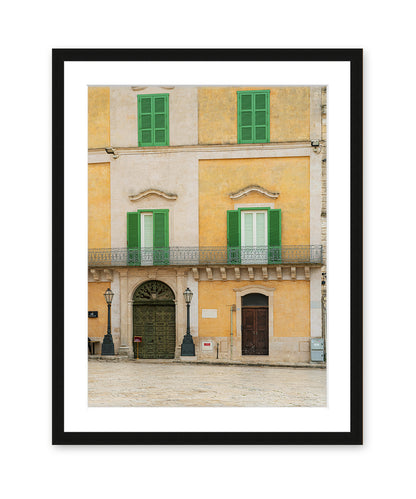 Fine art photograph in black frame featuring a historic building facade in Matera, Italy filled with soft beige, yellow, and green tones and architectural symmetry