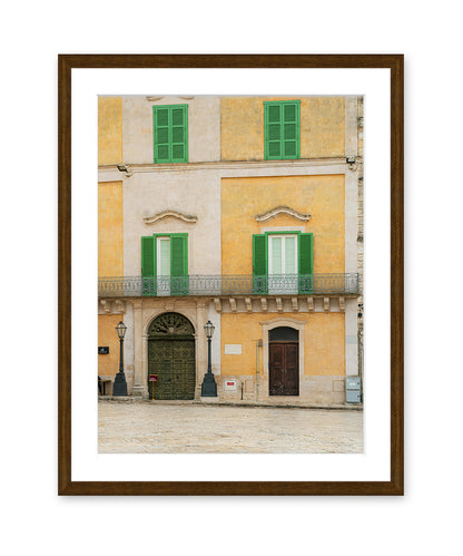 Fine art photograph in dark wood frame featuring a historic building facade in Matera, Italy filled with soft beige, yellow, and green tones and architectural symmetry