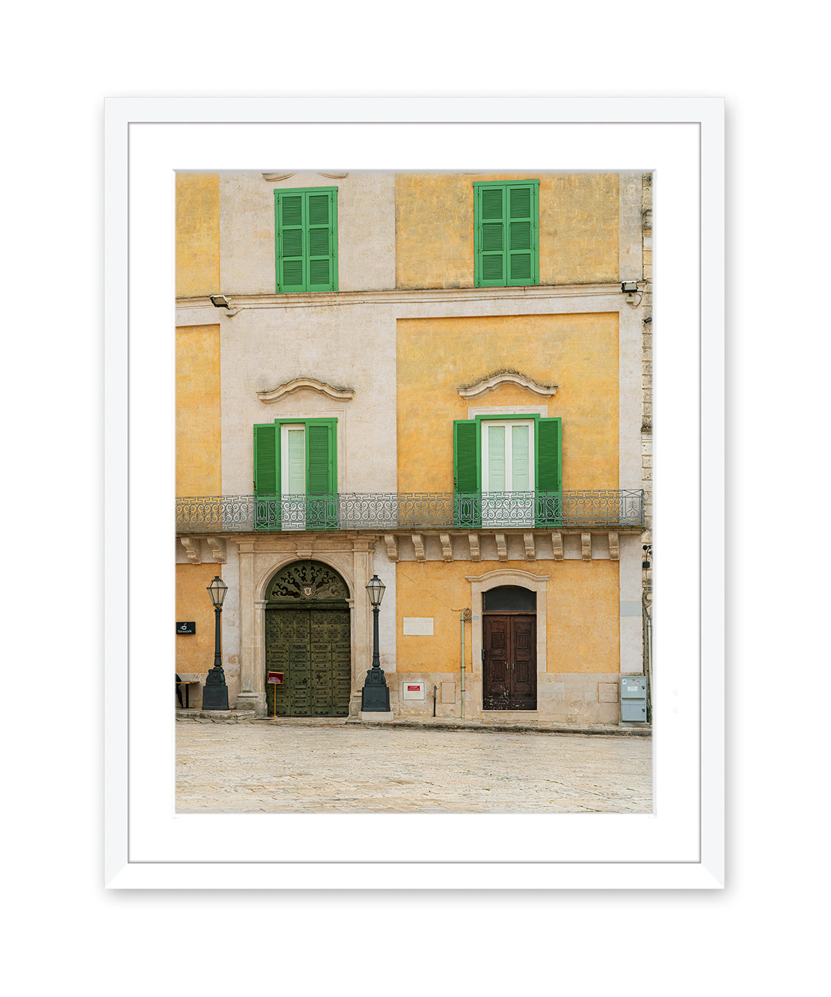Fine art photograph in white frame featuring a historic building facade in Matera, Italy filled with soft beige, yellow, and green tones and architectural symmetry